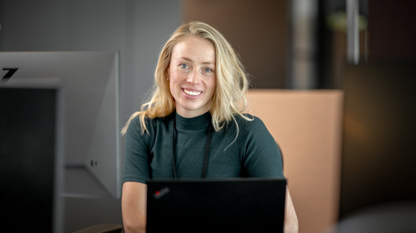 Kvinne foran pc smiler i kamera