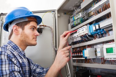 Elektriker med blå hjelm jobber med ledninger i et åpent elektrisk skap.