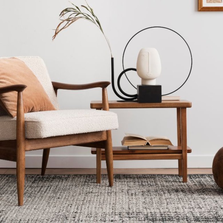Moderne stue med lenestol, bord, lampe og dekorasjoner i nøytrale farger.