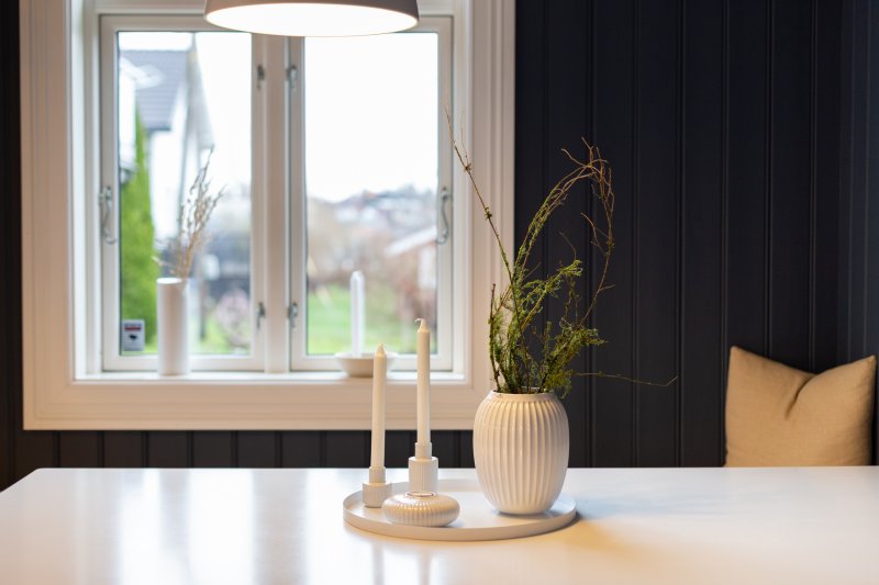 Moderne interiør med hvite lys og vase på et bord foran et vindu.