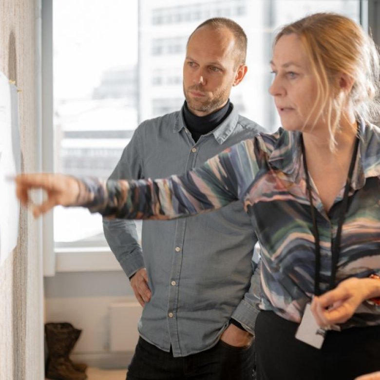 Tre personer diskuterer et prosjekt ved en tavle på et kontor.