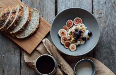 Frokost med brødskiver, yoghurt med frukt og nøtter, kaffe og melk på trebord.