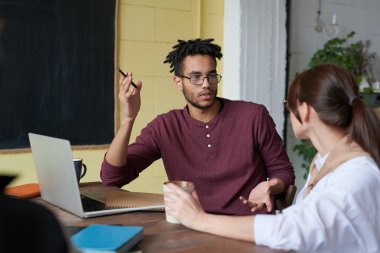 Person diskuterer med kollega ved et bord med laptop og notatbok.