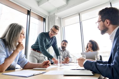 Personer i møte, diskuterer dokumenter rundt et bord i et moderne kontor.