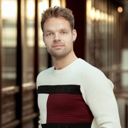 Mann i hvit genser står foran en bygning med glassvegger.