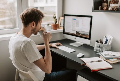 mann jobber med eksamen på pc hjemme med kaffekoppen i hånden