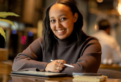 Dame som sitter foran en Ipad og smiler og ser inn i kamera