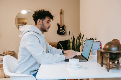 Mann jobber på laptop ved et bord med kaffekopp og globus.