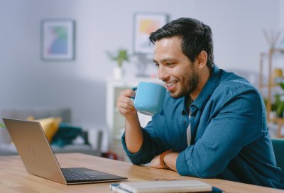 mann smiler og drikker kaffe og ser på pc skjerm