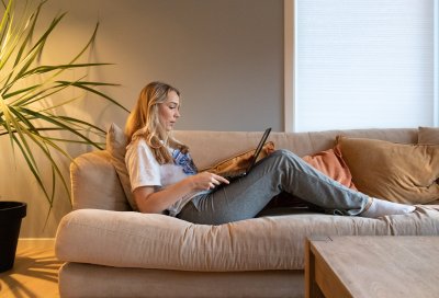 Kvinne sitter på sofaen med en bærbar datamaskin i et koselig hjemmemiljø.