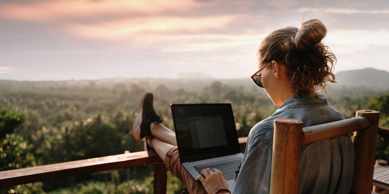 En kvinne sitter på verandaen med fin utsikt og jobber på PC
