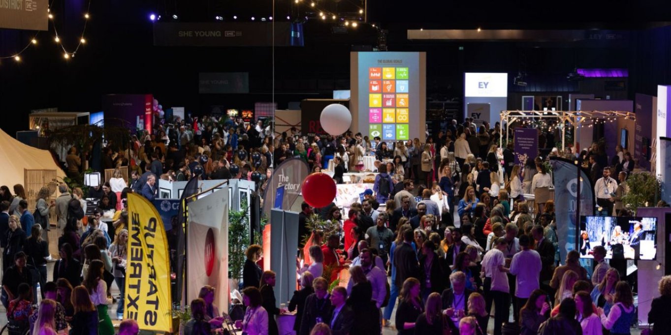 Mennesker på en travel messe med ulike stands og fargerike bannere.