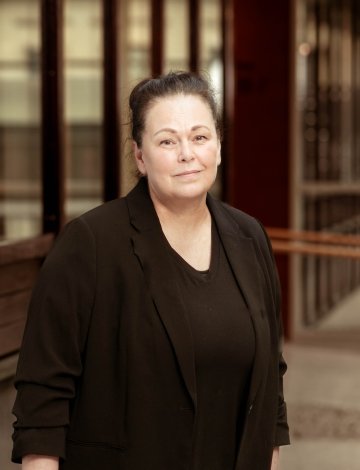 Kvinne i svart jakke står foran en bygning med glassvinduer og trepanel.