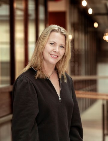Kvinne med langt blondt hår smiler i en moderne kontorbygning.