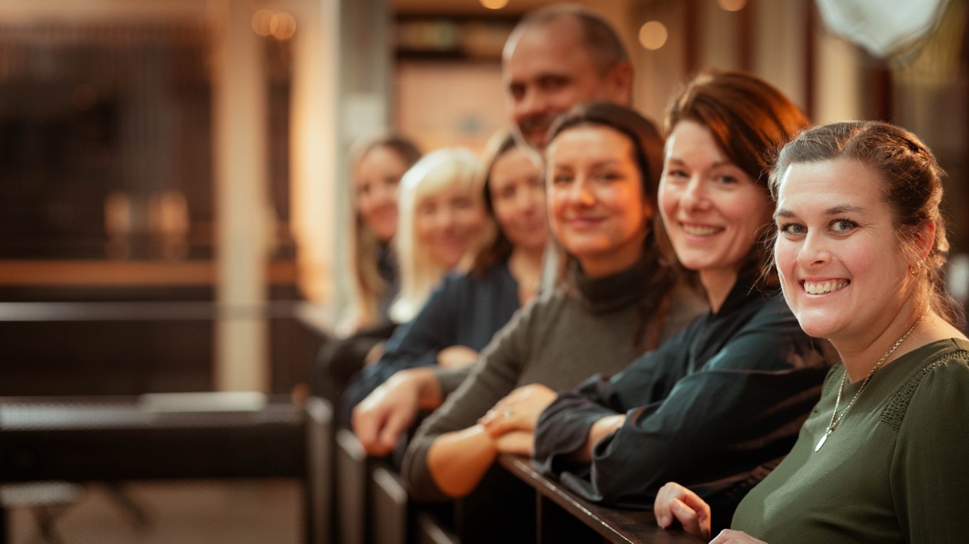 En gruppe smilende mennesker står på rekke innendørs.