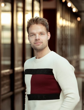 Mann i hvit genser står foran en bygning med glassvegger.
