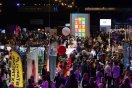 Mennesker på en travel messe med ulike stands og fargerike bannere.