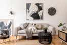 Stue med grå sofa, kunst på veggen, og en hund som ligger på sofaen.