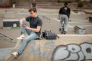 Ung mann sitter på rampen i skateparken og ser på mobilen sin.