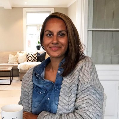 Kvinne smiler mens hun sitter i et stilfullt innredet rom med en kopp i hånden.