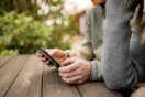 Person som bruker mobiltelefon ved et trebord utendørs.