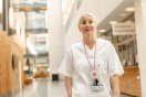 Sykepleier i hvit uniform står i en moderne sykehusgang.
