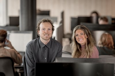 Madeleine Gjervan Hallum og Jo Eidsvold smiler og står foran en PC