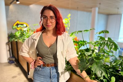 Kvinne med rødt hår står foran grønne planter i et moderne innendørs miljø.