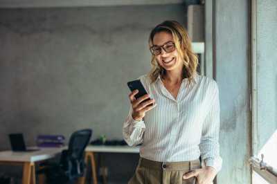 Kvinne smiler mens hun ser på mobilen i et kontor.