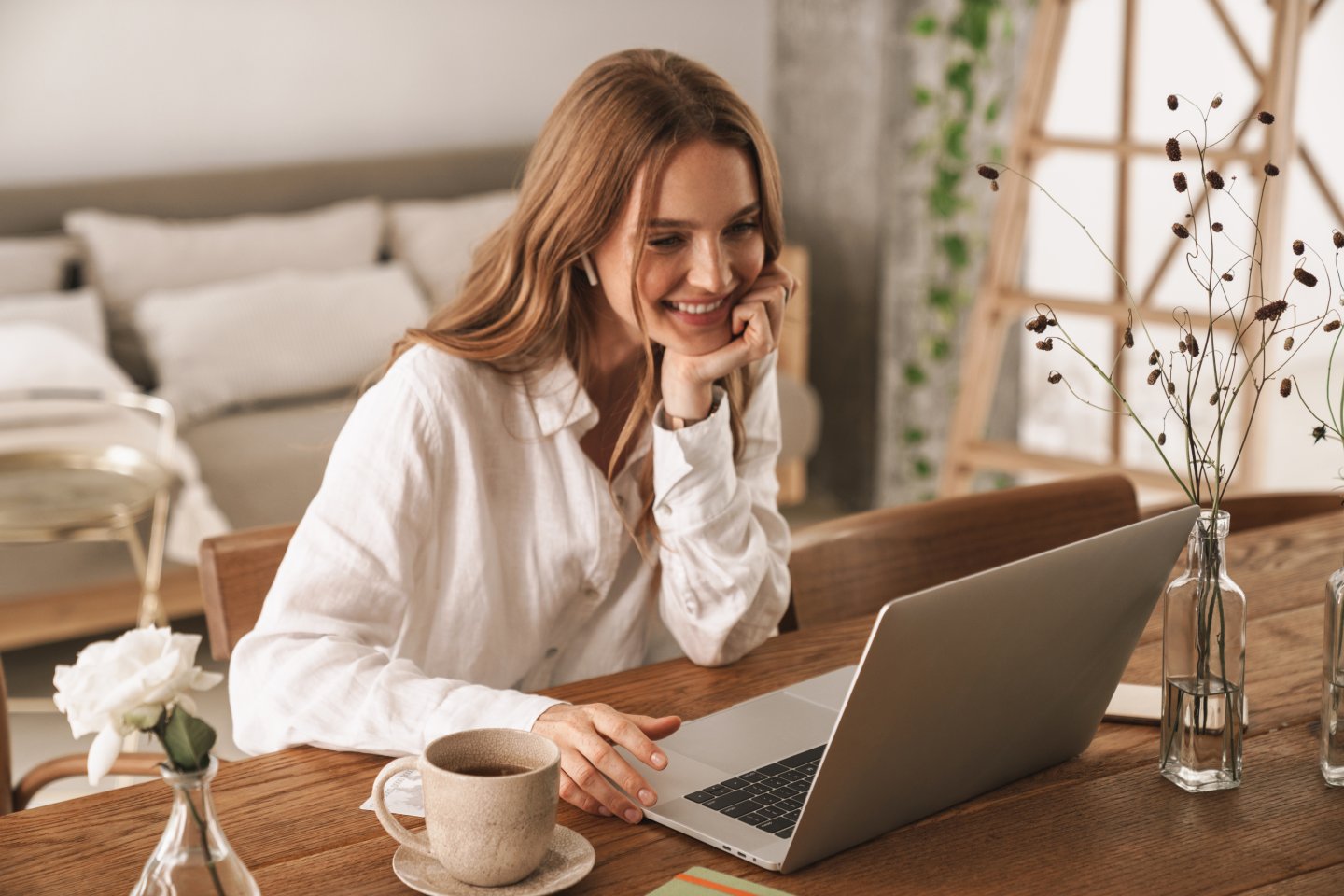 Smilende kvinne sitter hjemme og jobber på PC