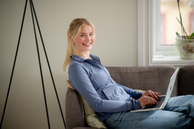 Ung kvinne jobber på PC mens hun sitter i sofaen