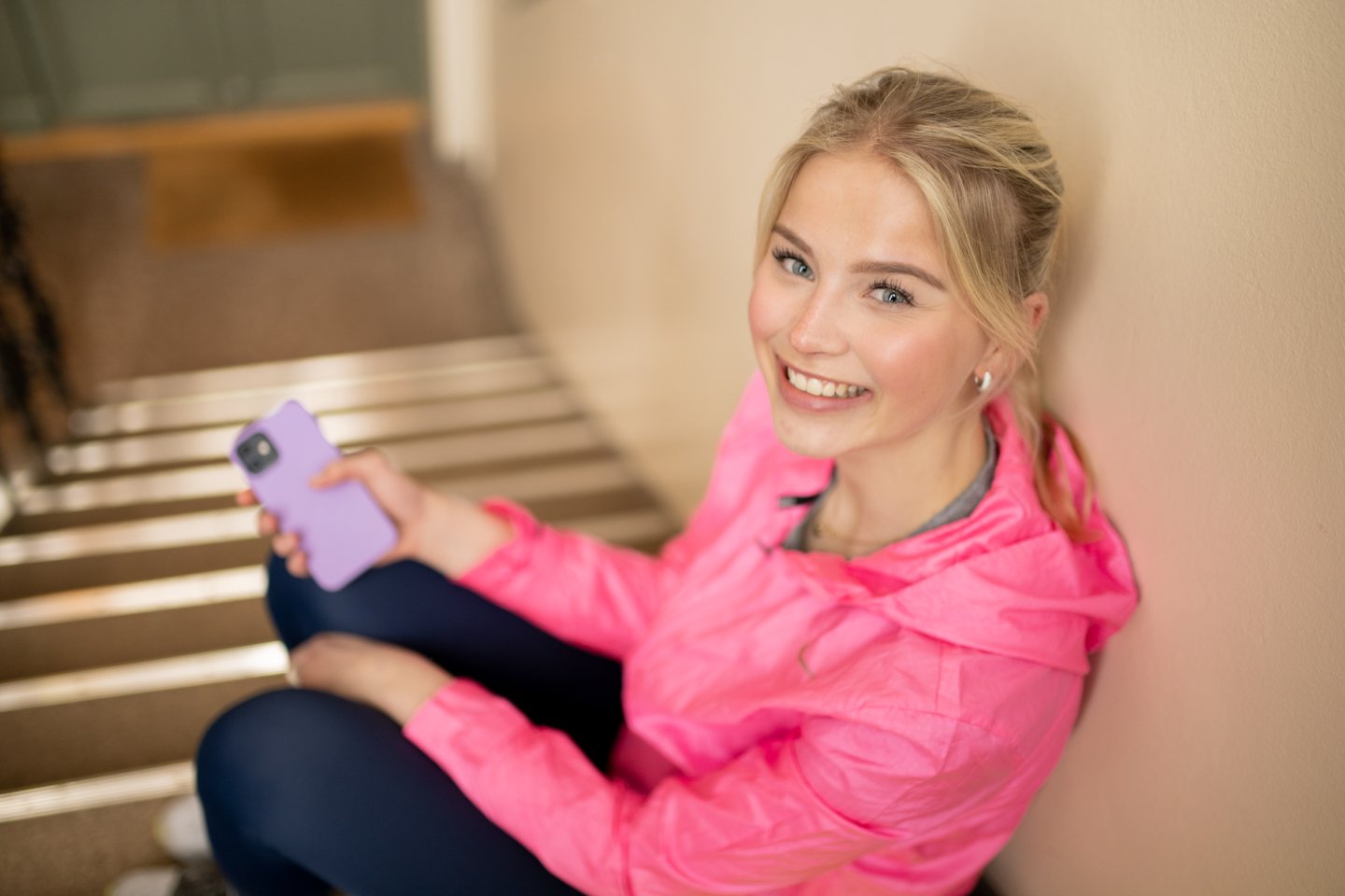 Ung kvinne sitter i trappen med mobilen og smiler til kameraet