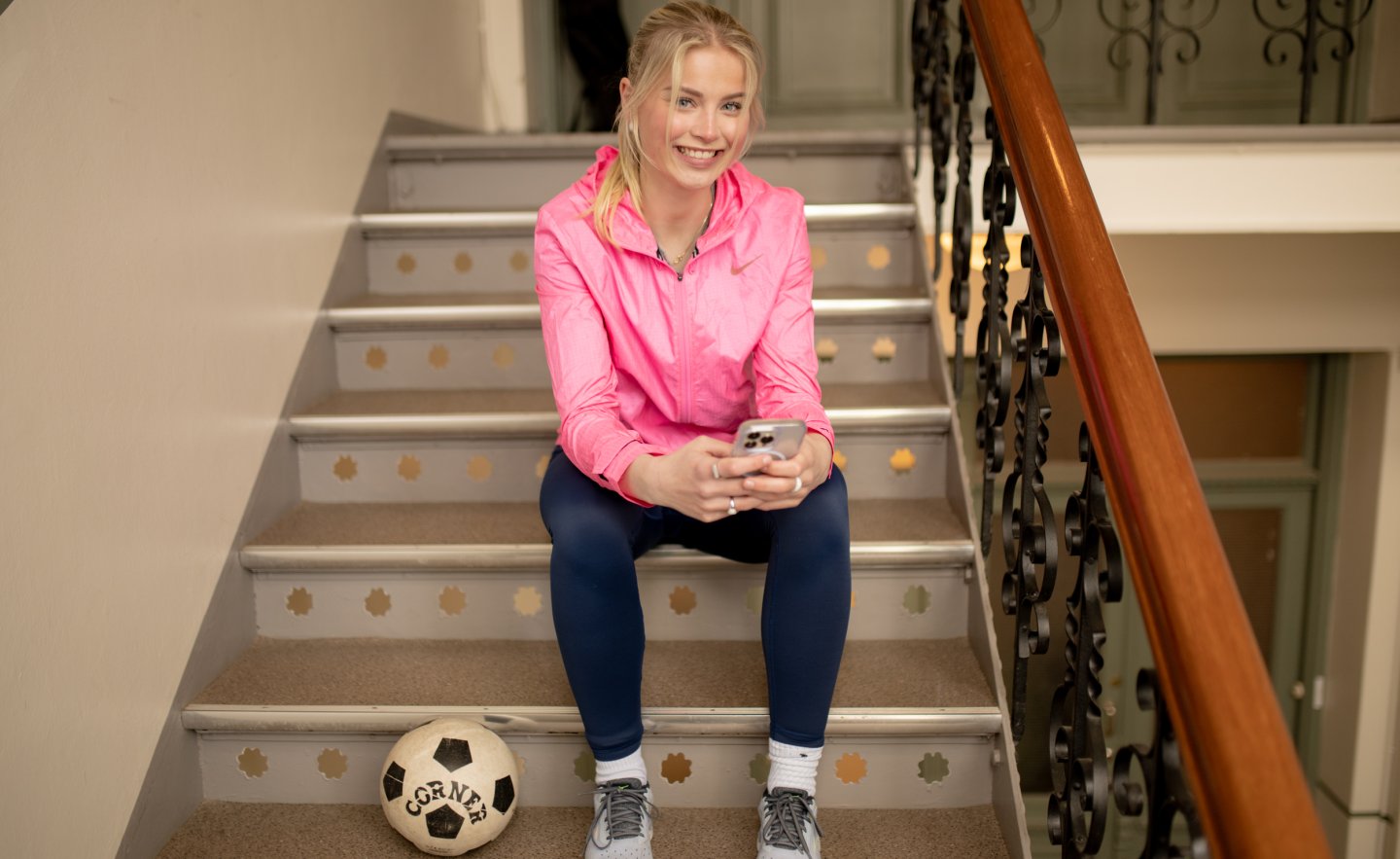 Smilende jente sitter i trappen med fotball og telefon