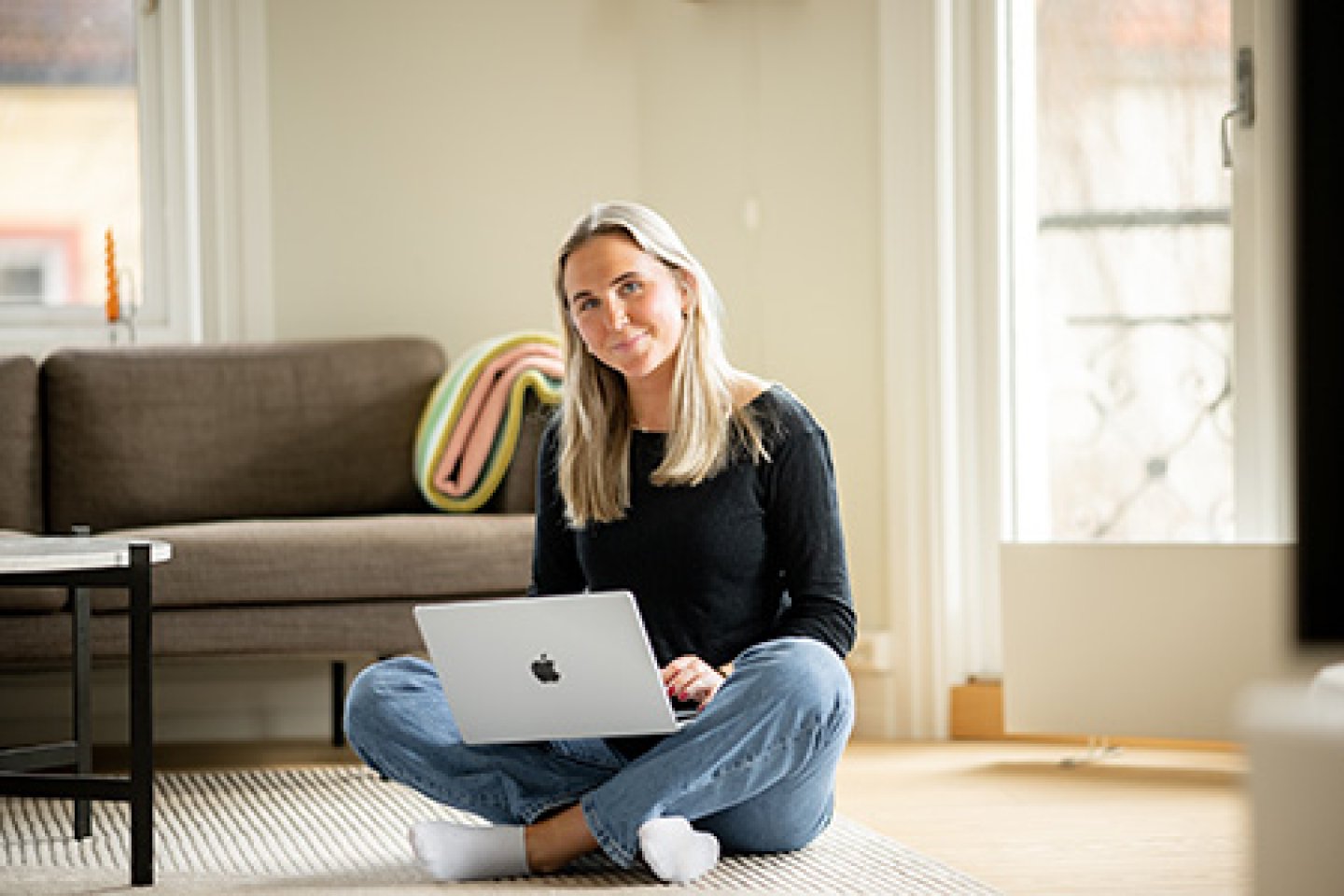 Ung kvinne sitter på gulvet i stua og jobber på PC