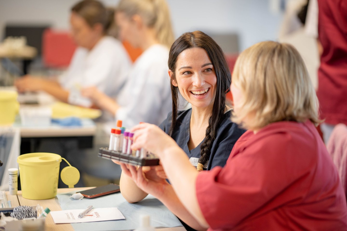 To smilende kvinnelige studenter øver seg på blodprøvetakning 