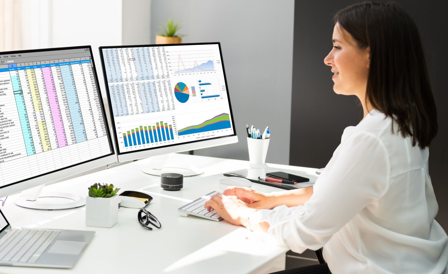 kvinnelig regnskapsmedarbeider jobber med excel ark på to datamaskiner