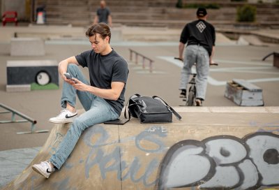 Ung mann sitter på rampen i skateparken og ser på mobilen sin.