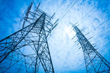 To høye elektriske kraftledninger mot en blå himmel med skyer.