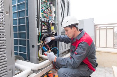 En elektriker i arbeid med et elektrisk skap utendørs, iført verneutstyr.
