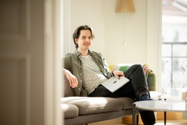 Person sitter på sofa med laptop i solfylt rom.