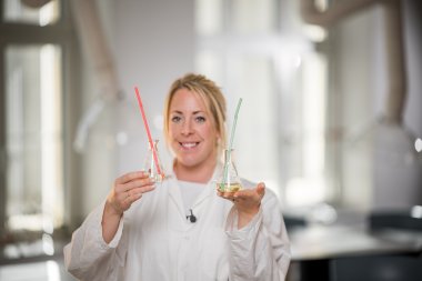 Kvinne i laboratoriefrakk holder to kolber med fargede væsker.