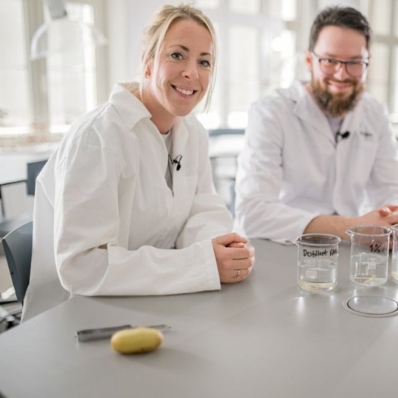 To personer i labfrakker med kjemikalier på et laboratoriebord.