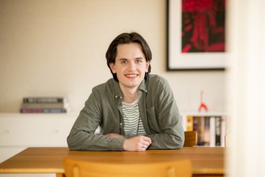 Person smiler ved et bord med bøker i bakgrunnen.