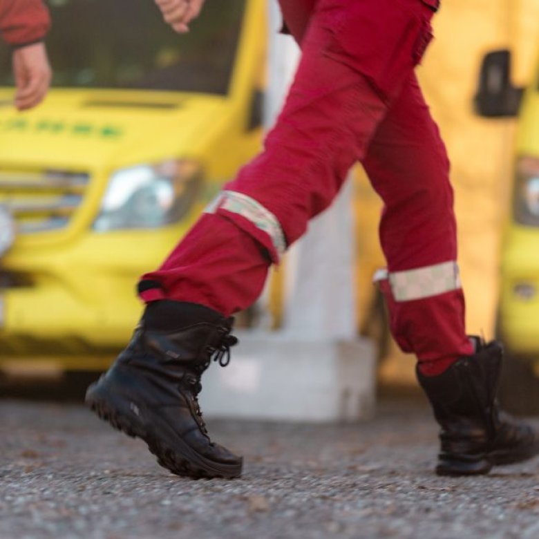 Ambulansepersonell i røde uniformer foran en gul ambulanse.