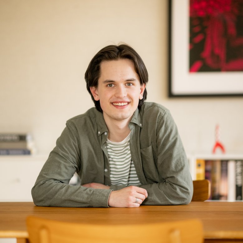 Ung mann smiler ved et bord i et moderne interiør.