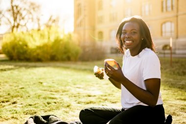 Kvinne smiler og spiser frukt i en solfylt park.