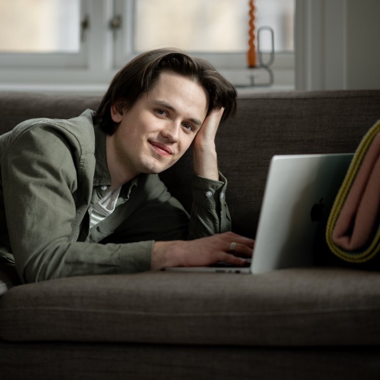 Person som ligger på sofaen og jobber på en bærbar datamaskin.