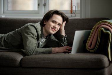 Person som ligger på sofaen og jobber på en bærbar datamaskin.