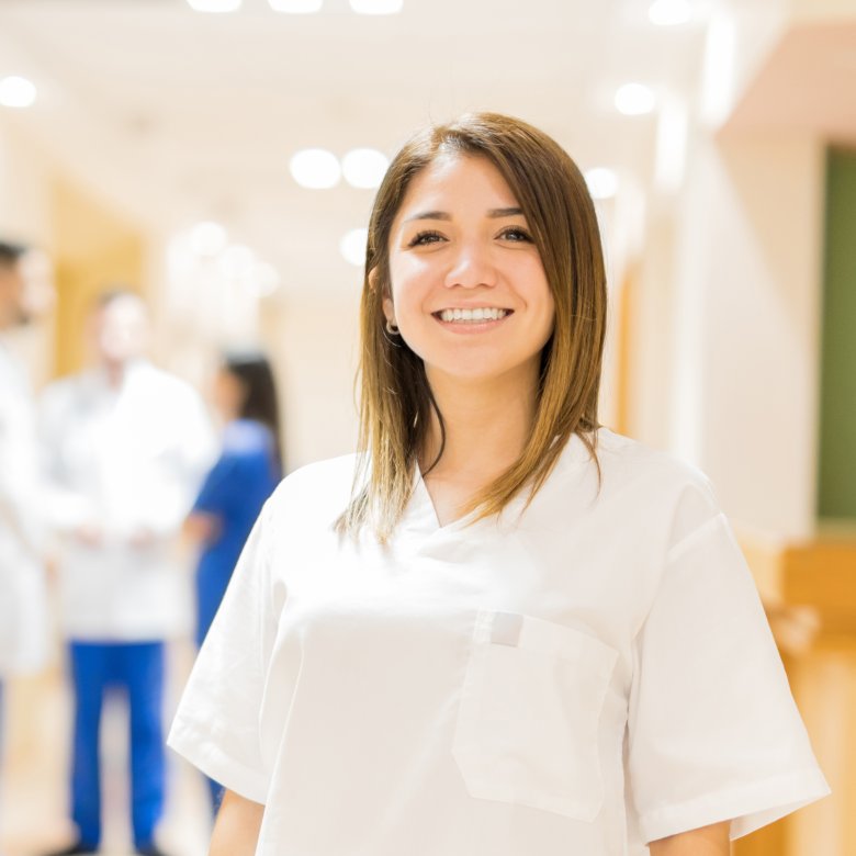 Smilende helsearbeider i hvit uniform på en klinikk med kolleger i bakgrunnen.
