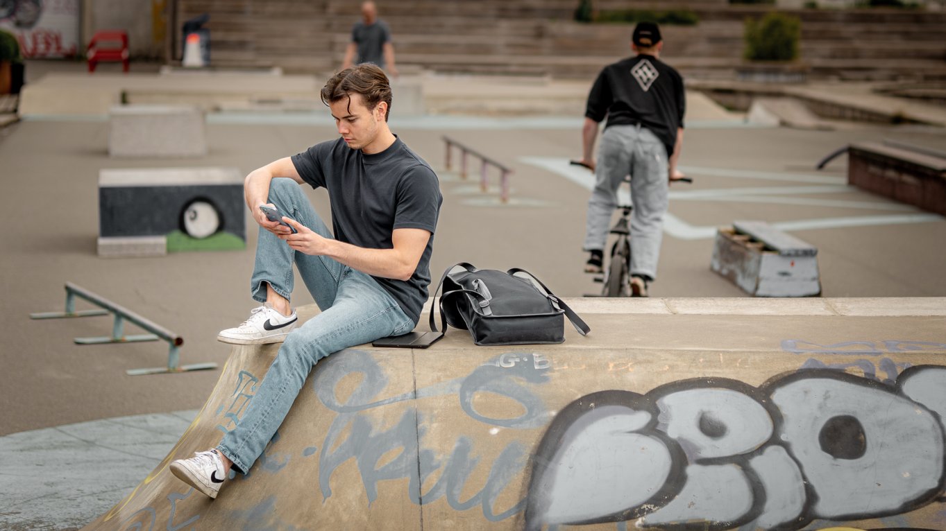 Ung mann sitter på rampen i skateparken og ser på mobilen sin.
